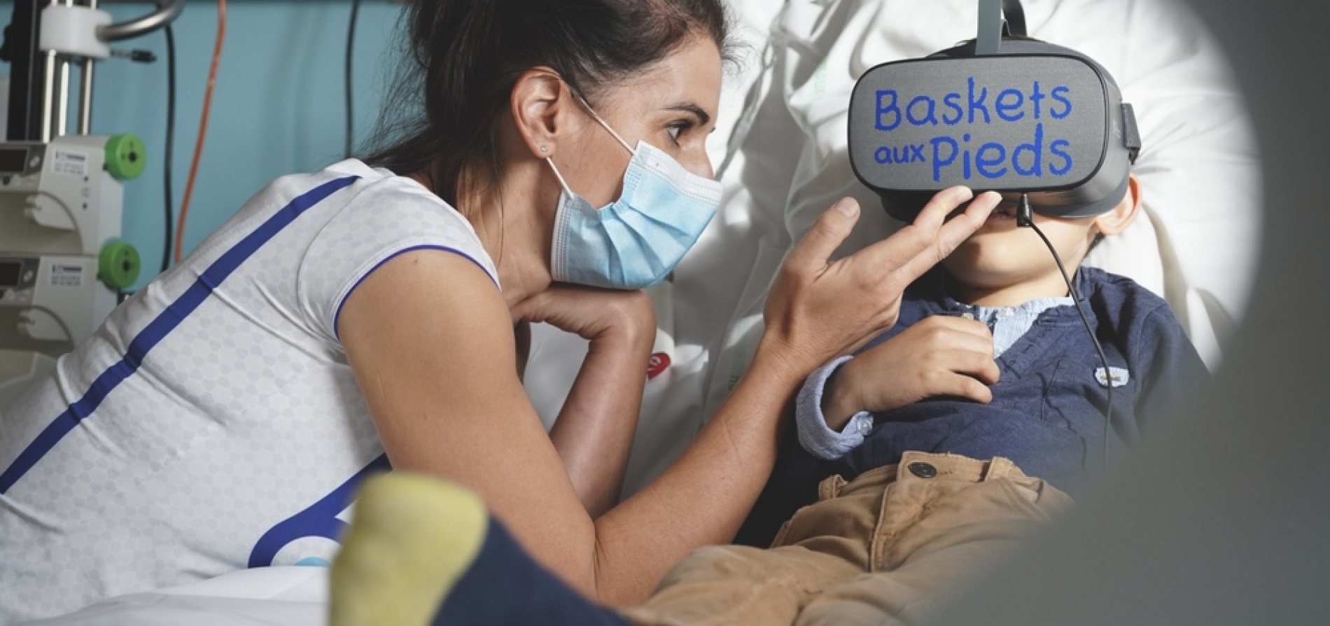 Photo d'un enfant hospitalisé avec un casque de réalité virtuelle de l'association Baskets aux Pieds, accompagné d'une soignante.