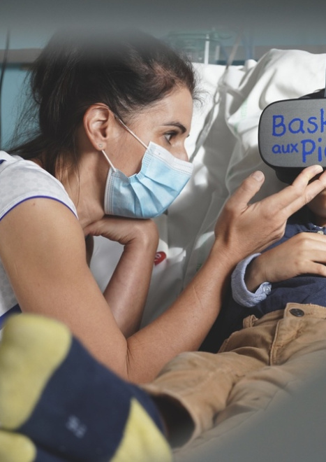 Photo d'un enfant hospitalisé avec un casque de réalité virtuelle de l'association Baskets aux Pieds, accompagné d'une soignante.